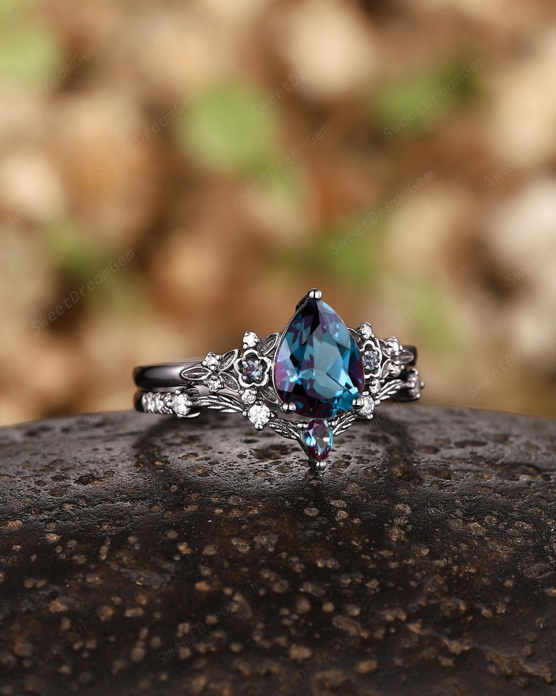 May include: A pear-shaped, blue-green gemstone ring with a silver band and a delicate floral design. The ring is set with smaller white gemstones.