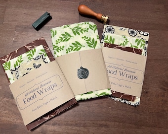 May include: Three sets of beeswax food wraps in various patterns. The wraps are made of fabric and are reusable and biodegradable. The packaging is brown paper with the text "All-Natural Beeswax Food Wraps from Baba Yaga's Hutch".