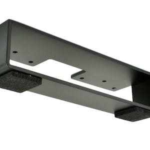 May include: A black metal bracket with a rectangular shape, featuring a cut-out section and several screw holes. Two dark gray foam pads are attached to the bottom. The bracket is designed for mounting.