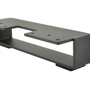 May include: A matte black metal bracket with a unique cut-out design. The bracket has a rectangular base with a raised, angled top section. Several holes are drilled for mounting. The overall design is modern and industrial.