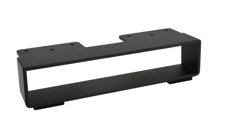 May include: A black metal bracket with a rectangular design. The bracket has a flat top with pre-drilled holes and a lower shelf. The overall shape is a long rectangle with an open center.