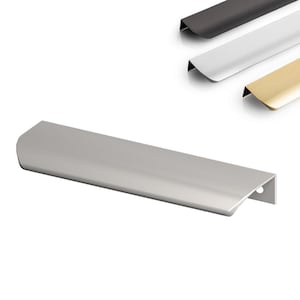Op de afbeelding: Een zilverkleurige kastgreep met een gebogen ontwerp. De greep is rechthoekig met een klein gaatje aan één uiteinde. Drie extra grepen in zwart, wit en goud zijn zichtbaar op de achtergrond.