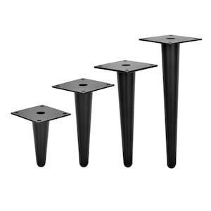 Può includere: Quattro gambe per mobili in metallo nero di diverse altezze. Le gambe sono affusolate e hanno una base quadrata.