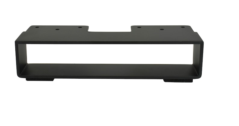 May include: A black metal shelf with a rectangular design. The shelf has a flat top with four holes and a lower shelf. The sides are solid, and the bottom has two small rectangular feet.