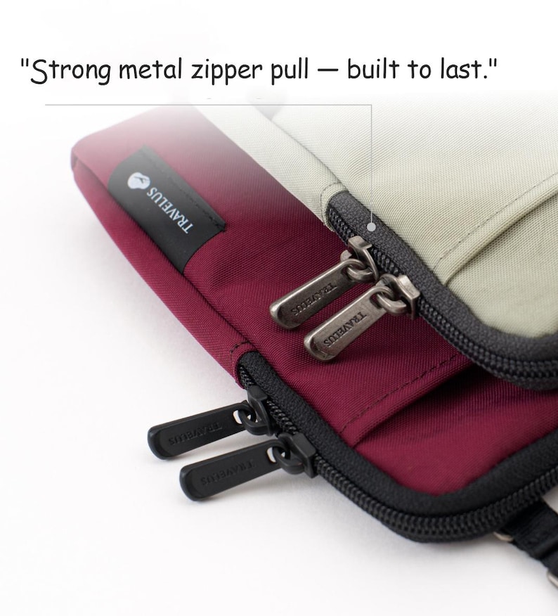 K&ouml;nnte beinhalten: Nahaufnahme eines weinroten und beigefarbenen Reiseaccessoires mit einem schwarzen Rei&szlig;verschluss. Die Metall-Rei&szlig;verschlussanh&auml;nger sind mit "TRAVELUS" graviert. Der Text "Strong metal zipper pull - built to last." ist sichtbar.