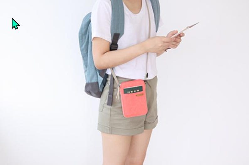 Puede incluir: Una bandolera de color coral con un acento verde y blanco se lleva alrededor del cuello. La bolsa es rectangular y tiene un peque&ntilde;o bolsillo. Una persona lleva la bolsa, una camiseta blanca, pantalones cortos caqui y una mochila azul.