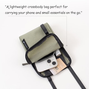 K&ouml;nnte beinhalten: Eine olivgr&uuml;ne Umh&auml;ngetasche mit schwarzem Rei&szlig;verschluss und Riemen. Die Tasche ist offen und zeigt ein Smartphone, eine Kreditkarte und kleine Kosmetikartikel. Der Text auf der Tasche lautet "TRAVELUS".