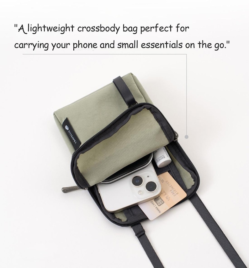 K&ouml;nnte beinhalten: Eine olivgr&uuml;ne Umh&auml;ngetasche mit schwarzem Rei&szlig;verschluss und Riemen. Die Tasche ist offen und zeigt ein Smartphone, eine Kreditkarte und kleine Kosmetikartikel. Der Text auf der Tasche lautet "TRAVELUS".