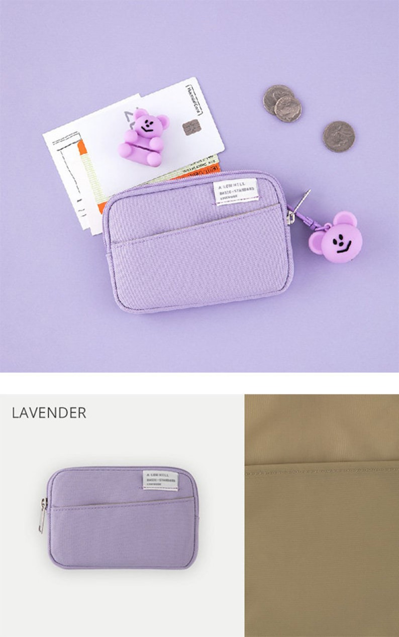Op de afbeelding: Een lavendelkleurige ritszak met een klein berenbedeltje. De tas heeft een klein vakje aan de voorkant en de tekst "A LITTLE BIT BASIC - STANDARD" staat gedrukt op een wit label.