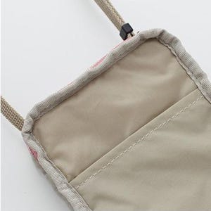 May include: A beige crossbody bag with a pink and white patterned design. The bag has a zipper closure and an inner pocket to store small items.
