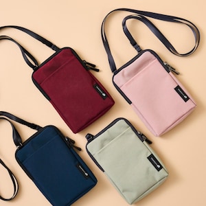 K&ouml;nnte beinhalten: Vier kleine Umh&auml;ngetaschen in den Farben Burgunderrot, Rosa, Marineblau und Salbeigr&uuml;n. Jede Tasche hat einen schwarzen Rei&szlig;verschluss, einen schwarzen Riemen und ein kleines Etikett mit der Aufschrift "TRAVELUS". Die Taschen sind aus einem glatten, strapazierf&auml;higen Material gefertigt.