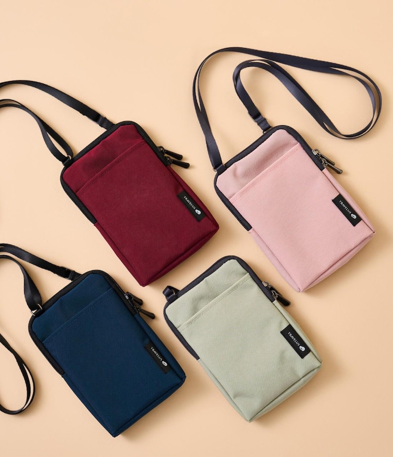 K&ouml;nnte beinhalten: Vier kleine Umh&auml;ngetaschen in den Farben Burgunderrot, Rosa, Marineblau und Salbeigr&uuml;n. Jede Tasche hat einen schwarzen Rei&szlig;verschluss, einen schwarzen Riemen und ein kleines Etikett mit der Aufschrift "TRAVELUS". Die Taschen sind aus einem glatten, strapazierf&auml;higen Material gefertigt.