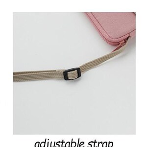 May include: A close-up of a light pink canvas bag with an adjustable strap. The strap is made of a beige fabric and has a black plastic buckle.