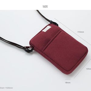 May include: A burgundy felt phone pouch with a zipper closure and a black adjustable strap. The pouch measures 5.7 inches wide, 4.1 inches tall, and 0.7 inches thick.