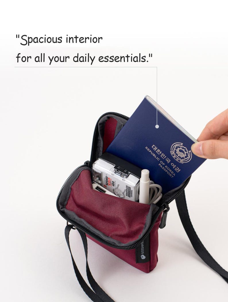 K&ouml;nnte beinhalten: Eine weinrote Umh&auml;ngetasche mit schwarzem Riemen, ge&ouml;ffnet, um einen Reisepass, eine Kamera und andere kleine Gegenst&auml;nde zu zeigen. Die Tasche tr&auml;gt den Text "Spacious interior for all your daily essentials."