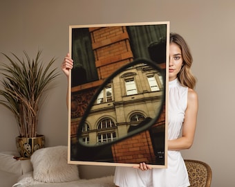 Könnte beinhalten: Ein gerahmter Druck mit einem Gebäude, das sich in einem Spiegel spiegelt. Das Gebäude hat gewölbte Fenster und eine hellfarbene Fassade. Der Rahmen ist hellbraun. Das Bild wird vor einer Person gehalten.