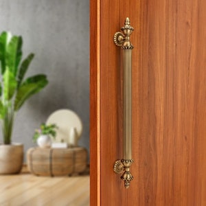 May include: A gold-toned door handle with a decorative design. The handle is attached to a wooden door.