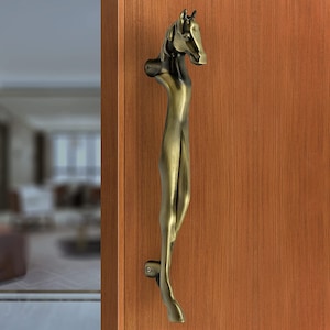 May include: A gold-toned door handle shaped like a horse's head and neck. The handle is mounted on a wooden door.