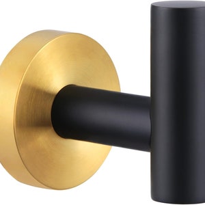 May include: A black and gold wall hook with a round base and a single hook. The hook is made of metal and has a brushed finish.