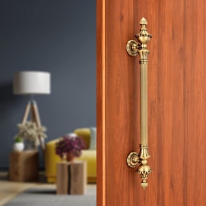 May include: A gold-toned door handle with an ornate design. The handle is attached to a wooden door.