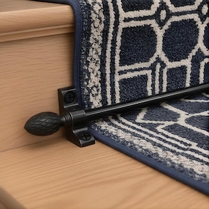 May include: Close-up of a navy blue and white patterned stair runner with a black metal stair rod. The runner has a geometric design and is installed on a wooden staircase. The rod has a decorative finial.