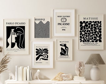 May include: A set of six black and white framed art prints featuring abstract designs and text. The prints are hung on a white wall with a white shelf below. The shelf has a white vase with dried flowers, a stack of books, two white ceramic animal figurines, a wicker basket with white beads, and a white ceramic sculpture.