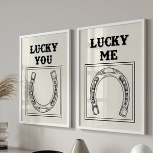 May include: Two white framed prints with black text and illustrations of horseshoes. The left print says "Lucky You" and the right print says "Lucky Me".