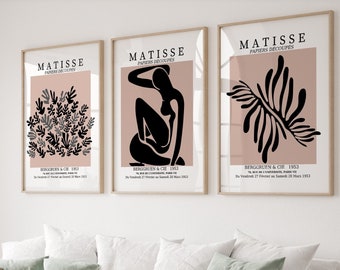 May include: Three framed prints of Matisse's "Papiers Decoupes" artwork. Each print features a different design in black and gray on a pink background. The text "MATISSE" and "PAPIERS DECOUPES" is printed in black at the top of each print. The text "BERGGRUEN & CIE 1953" is printed at the bottom of each print.