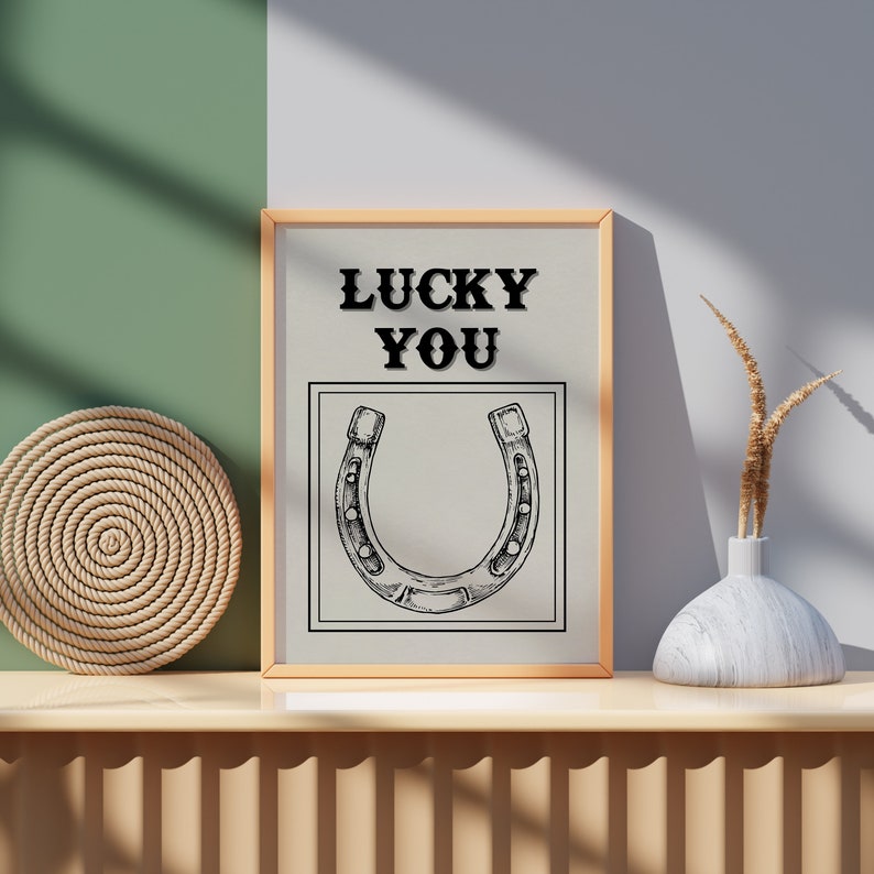 May include: A framed print with a horseshoe illustration and the text "LUCKY YOU" in black lettering on a beige background.