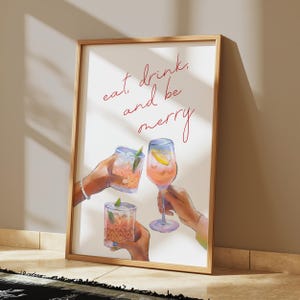 May include: A white framed print with the text "eat, drink, and be merry" in red cursive. Three hands are holding up glasses of pink and orange drinks.