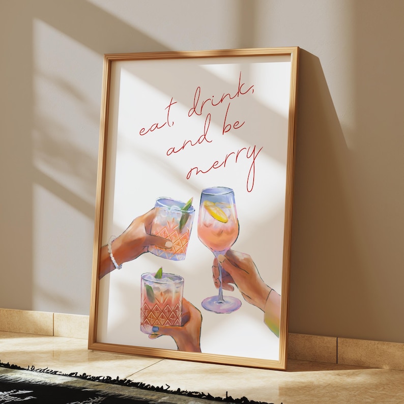 May include: A white framed print with the text "eat, drink, and be merry" in red cursive. Three hands are holding up glasses of pink and orange drinks.