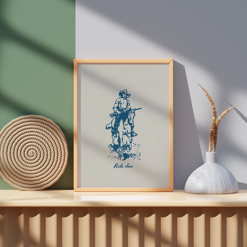 May include: A framed print with a blue illustration of a cowboy riding a horse. The text "Ride slow" is printed below the illustration.