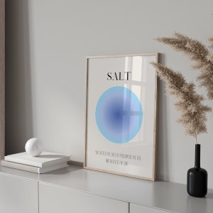May include: A framed print with a blue gradient circle and the word "SALT" in black text. The text below the circle reads "She tasted the salt of freedom in the sea and reveled in the sun."