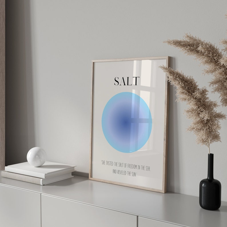 May include: A framed print with a blue gradient circle and the word "SALT" in black text. The text below the circle reads "She tasted the salt of freedom in the sea and reveled in the sun."