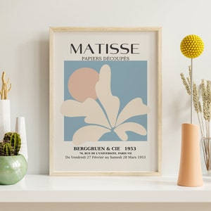 Pu&ograve; includere: Una stampa incorniciata di un'opera d'arte di Matisse intitolata "PAPIERS D&Eacute;COUP&Eacute;S". L'opera d'arte presenta un fiore stilizzato con un cerchio rosa sullo sfondo. Il testo "BERGGRUEN & CIE 1953" &egrave; nella parte inferiore della stampa, insieme all'indirizzo "70, RUE DE L'UNIVERSITE, PARIS VII" e alle date "Du Vendredi 27 F&eacute;vrier au Samedi 28 Mars 1953".
