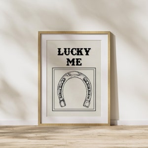 May include: A framed print with the text "LUCKY ME" and a black and white illustration of a horseshoe.