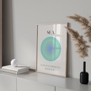 May include: A framed print with a blue and green gradient circle and the word "SEA" in black text. The text below the circle reads "She tasted the salt of freedom in the sea, and reveled in the sun."