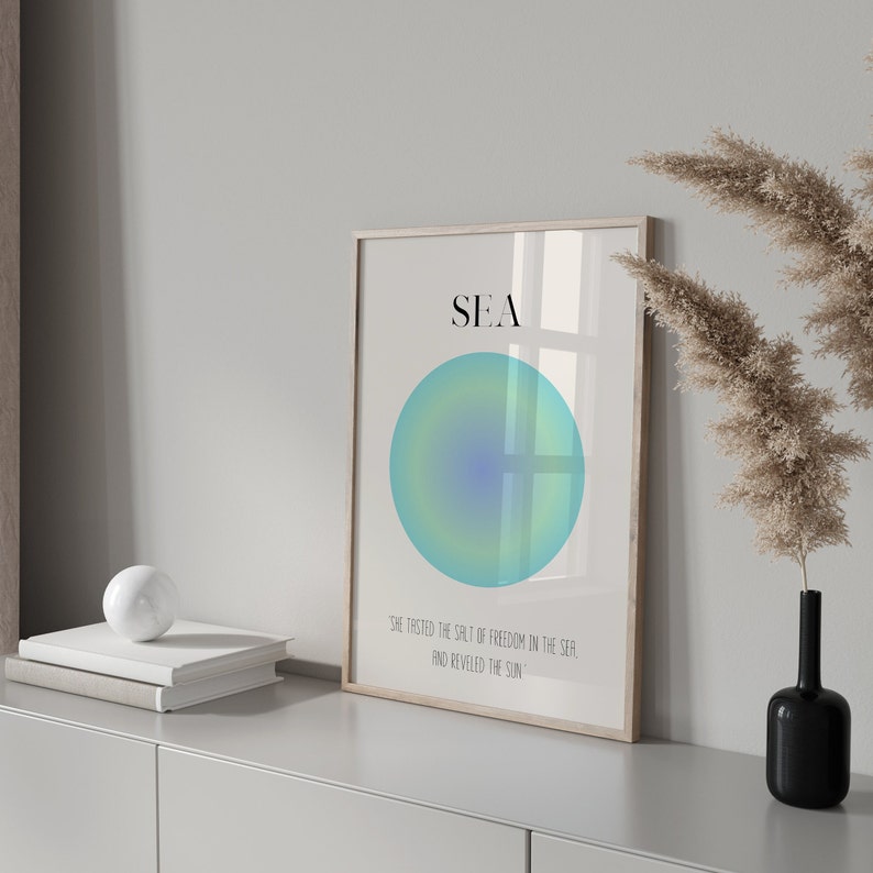 May include: A framed print with a blue and green gradient circle and the word "SEA" in black text. The text below the circle reads "She tasted the salt of freedom in the sea, and reveled in the sun."