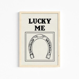 May include: A framed print with a black and white illustration of a horseshoe and the text "LUCKY ME" in black.