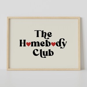 May include: A framed print with a beige background and black text that reads "The Homebody Club" with two red hearts.