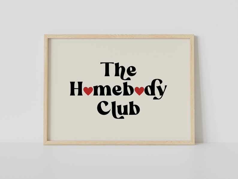 May include: A framed print with a beige background and black text that reads "The Homebody Club" with two red hearts.