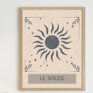 May include: A framed print with a beige background and a stylized blue sun with rays. The sun is surrounded by small white stars. The print has a border with a leafy design in the corners and the text "LE SOLEIL" at the bottom.