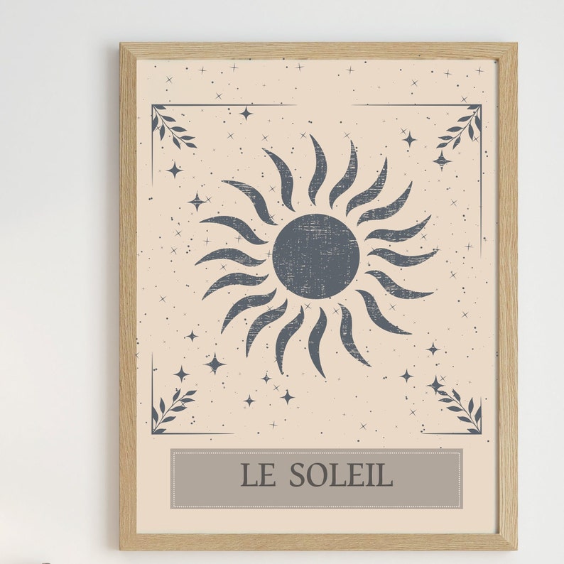 May include: A framed print with a beige background and a stylized blue sun with rays. The sun is surrounded by small white stars. The print has a border with a leafy design in the corners and the text "LE SOLEIL" at the bottom.