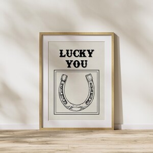 May include: A framed print with a black and white illustration of a horseshoe and the text "LUCKY YOU" in black.