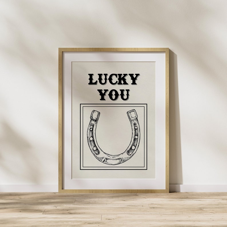 May include: A framed print with a black and white illustration of a horseshoe and the text "LUCKY YOU" in black.