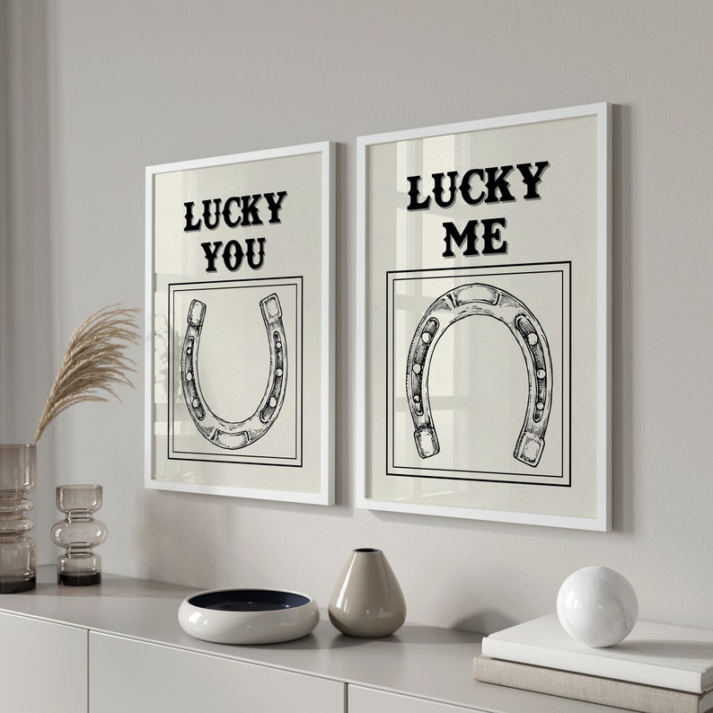 May include: Two white framed prints with black text and illustrations of horseshoes. The left print says "Lucky You" and the right print says "Lucky Me".