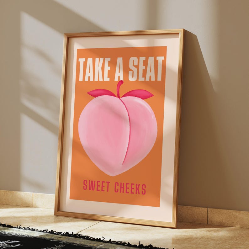 May include: A peach-colored poster with the text "Take a Seat" in white letters and "Sweet Cheeks" in pink letters. A pink peach with a green stem and red leaves is in the center of the poster.