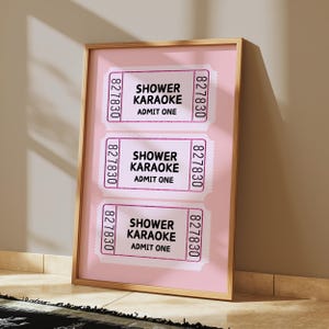 May include: Three pink ticket stubs with the text "Shower Karaoke" and "Admit One" printed on each. The tickets are framed and displayed on a pink background.