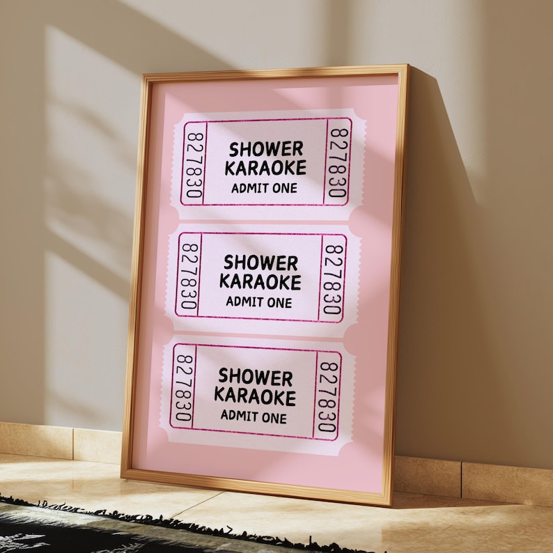 May include: Three pink ticket stubs with the text "Shower Karaoke" and "Admit One" printed on each. The tickets are framed and displayed on a pink background.