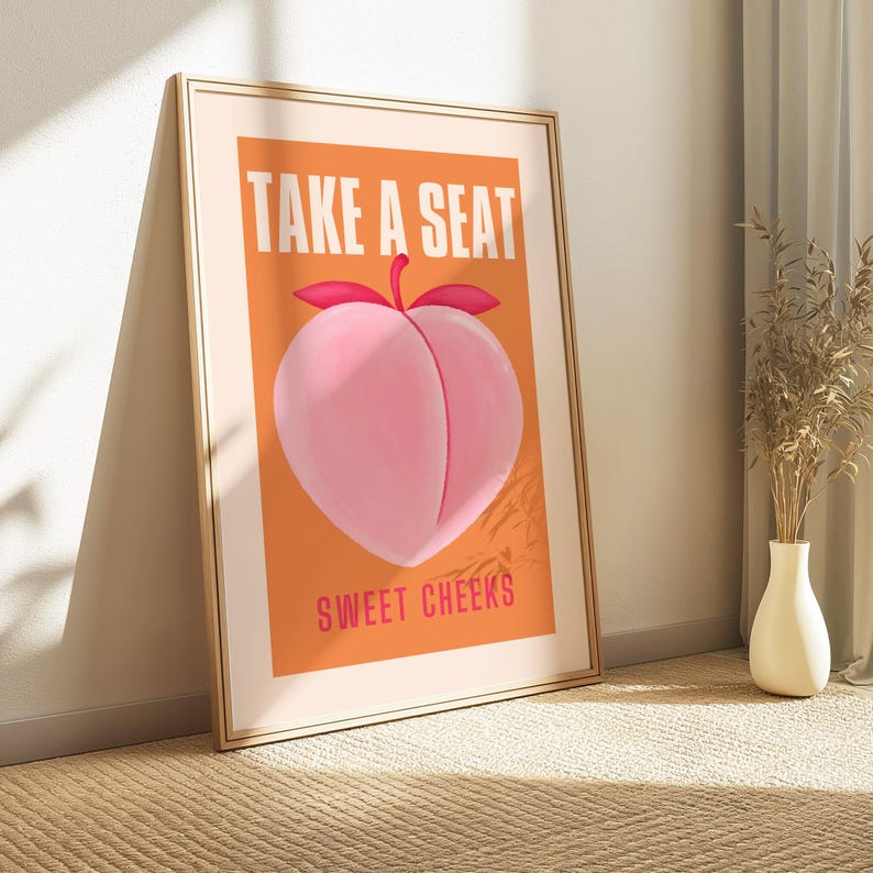 May include: A peach-colored poster with the text "Take a Seat" in white letters and "Sweet Cheeks" in pink letters. A peach with a green stem and leaves is in the center of the poster.